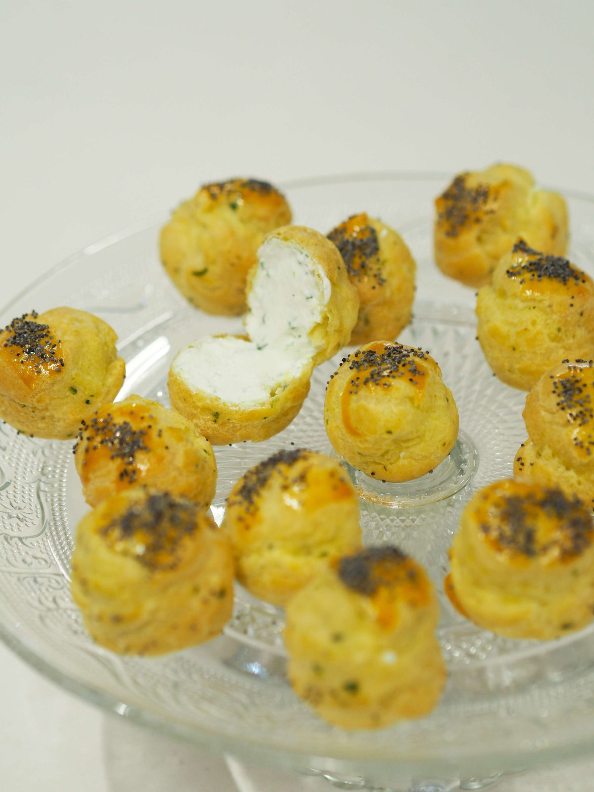 Golden gougères topped with poppy seeds, filled with seasoned whipped cream, arranged on a serving board