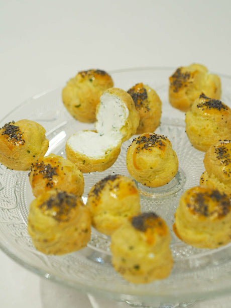Golden gougères topped with poppy seeds, filled with seasoned whipped cream, arranged on a serving board