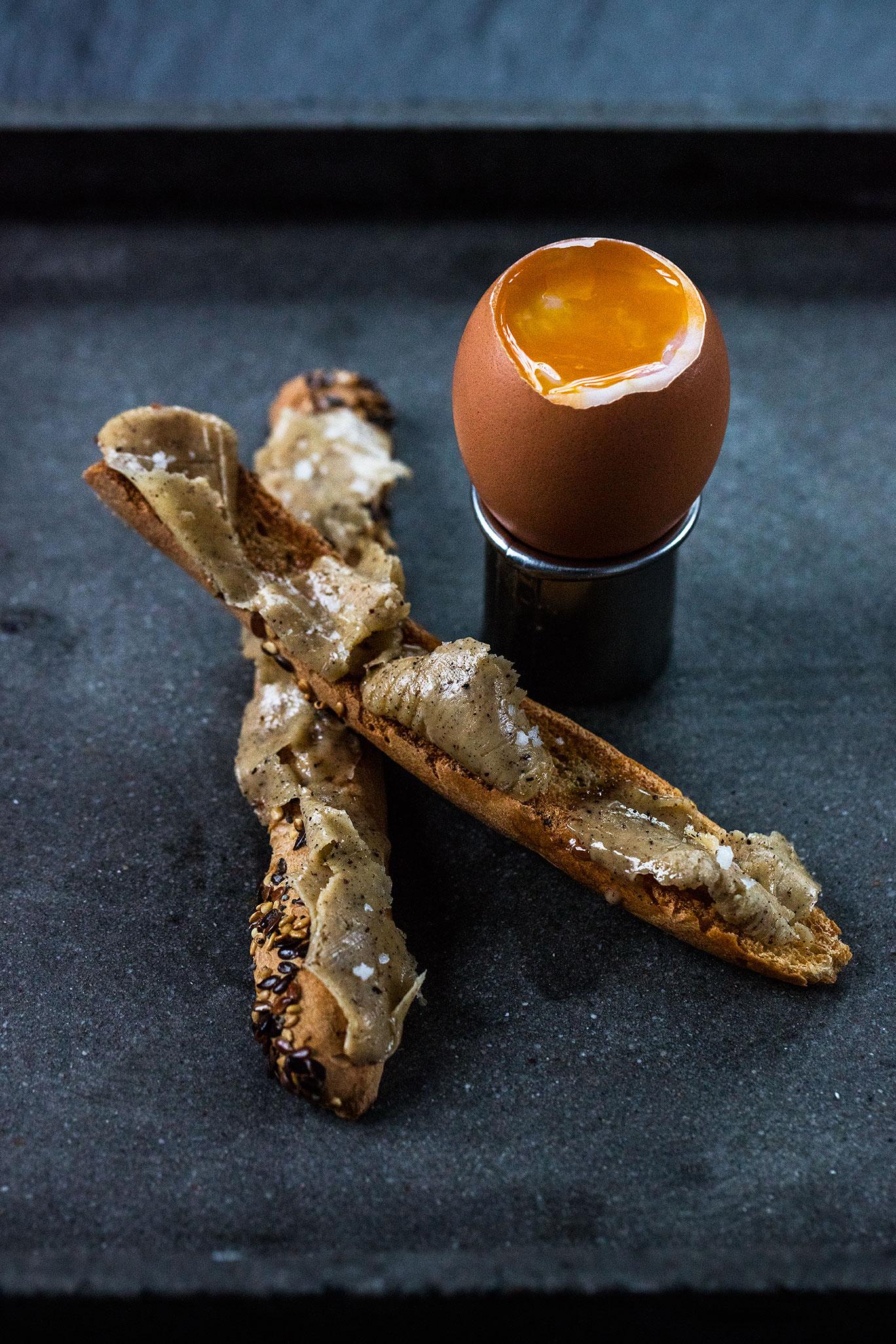 A soft-boiled egg in an egg cup with toasted baguette soldiers spread with vanilla butter