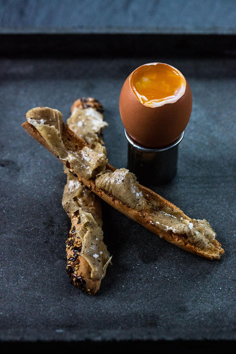 A soft-boiled egg in an egg cup with toasted baguette soldiers spread with vanilla butter