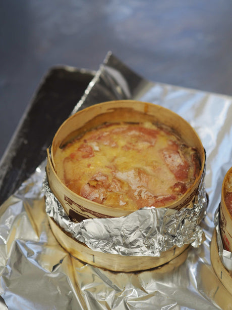 A whole baked Vacherin du Haut-Doubs in its spruce box, rind golden and cheese melted