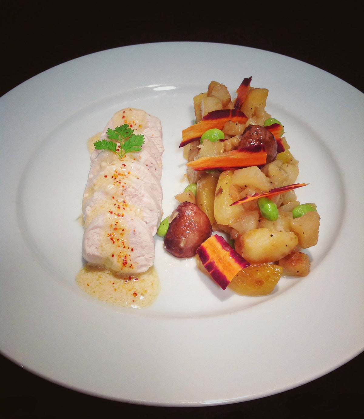 Sliced chicken ballotine plated with glazed seasonal root vegetables and a creamy onion butter sauce