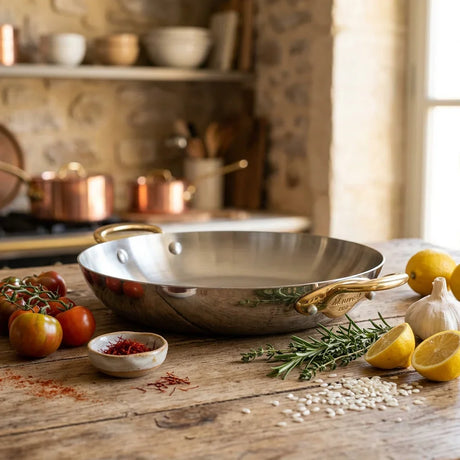Mauviel stainless steel skillet on a wooden table with lemons, garlic, and spices
