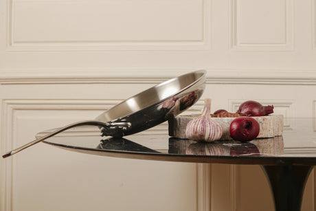 Stainless steel frying pan and red onions on a dark table.