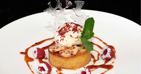 French dessert with cake, ice cream, fresh raspberries, caramel sauce, and mint garnish