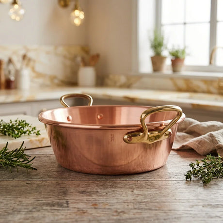 A polished copper cooking pot with brass handles on a rustic wooden countertop.