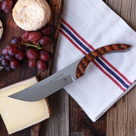 André & Michel Bras cheese knife with a wooden handle resting on a white cloth towel.