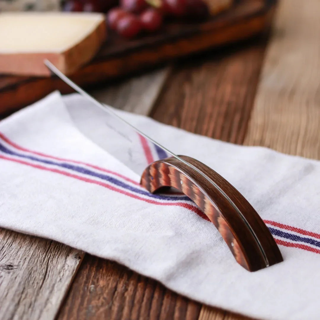 A cheese knife with a curved wooden handle resting on a white cloth napkin with red stripes.