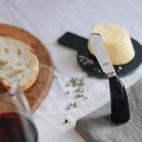 Black horn handle butter knife with artisanal butter, sliced bread, wine, and peppercorns