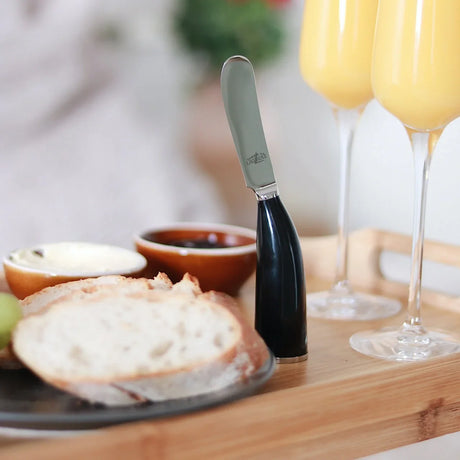 A Laguiole spreader knife with a black handle standing upright on a wooden tray.