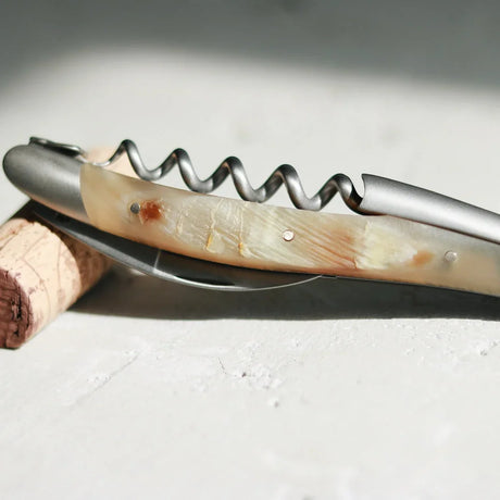 A silver metal corkscrew with a cream-colored horn handle resting on a wine cork.