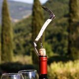 A white handled wine opener with a corkscrew and knife inserted into a wine bottle cap.