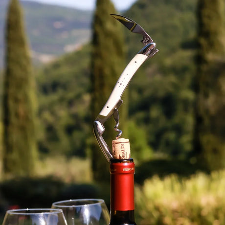 A white handled wine opener with a corkscrew and knife inserted into a wine bottle cap.