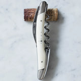 Silver waiter's corkscrew with a white handle resting on a wine cork over marble.