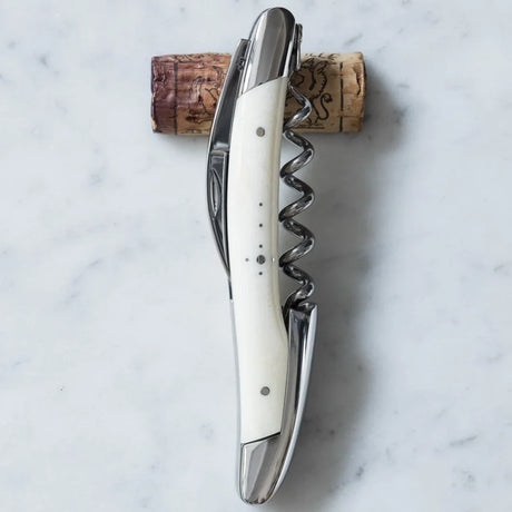 Silver waiter's corkscrew with a white handle resting on a wine cork over marble.