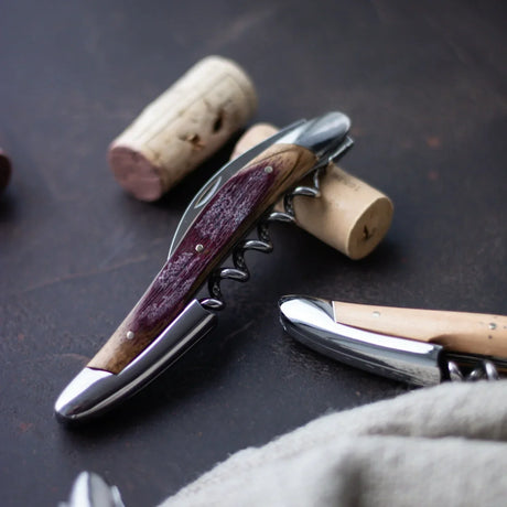 Stainless steel corkscrew wine opener with a dark wood handle on a dark surface.