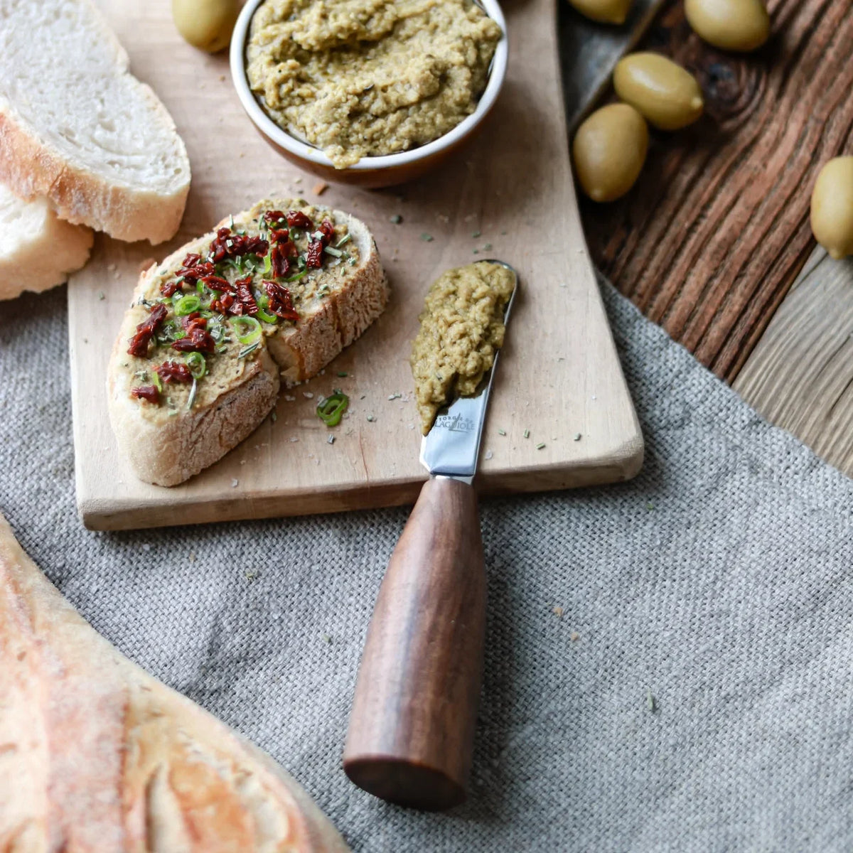 Toasted bread topped with olive tapenade and sun-dried tomatoes on a wooden board.