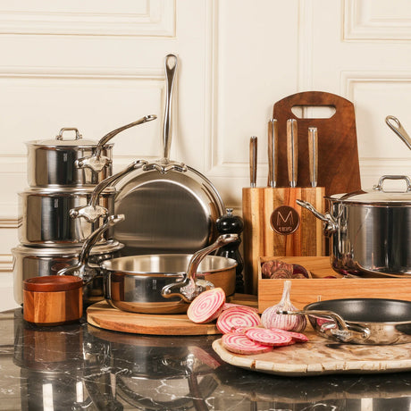 Stainless steel cookware set with various pots and pans on a marble countertop.