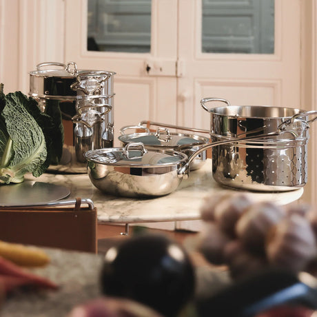 Stainless steel pots, pans, and a colander set on a marble tabletop.