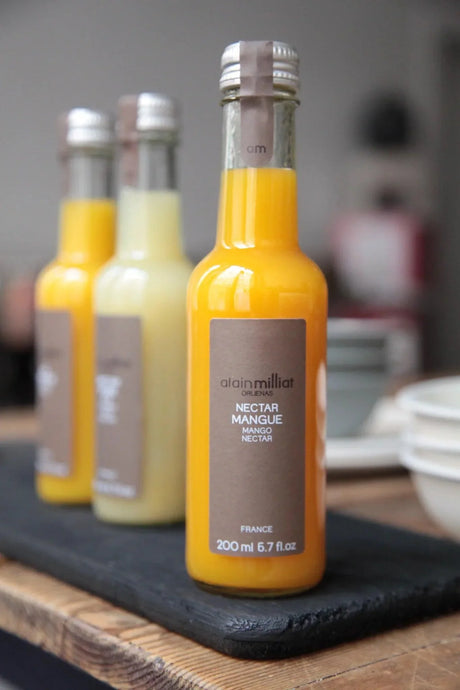 Alain Milliat mango nectar bottle, premium French fruit juice, on rustic wooden table