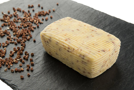 Artisan French buckwheat butter block with grains on black slate, premium imported pantry item