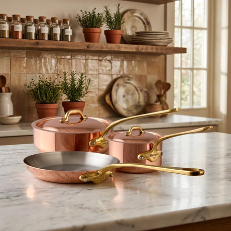 Mauviel copper cookware set including a pan, pot, and lid on a marble countertop.