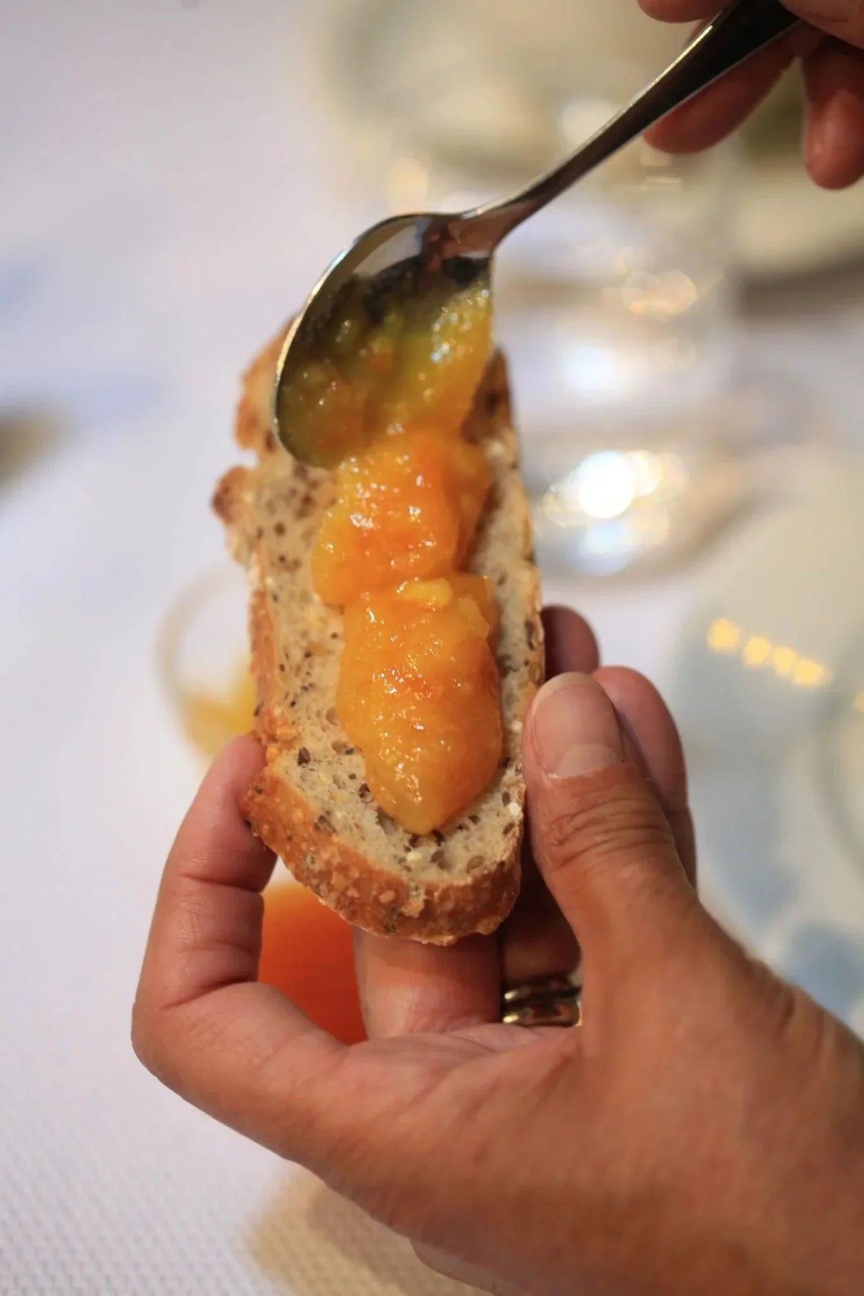 Hand spreading artisan French jam on seeded bread slice, gourmet breakfast or charcuterie board