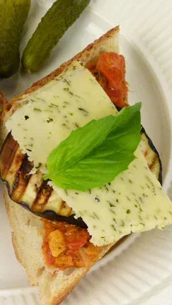 Rustic baguette with herbed cheese, grilled eggplant, tomatoes, and fresh basil garnish.