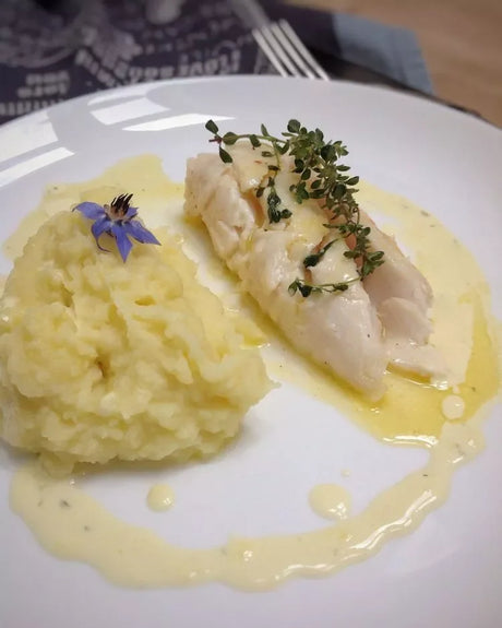 French cod fillet with mashed potatoes and butter sauce, garnished with herbs on a white plate