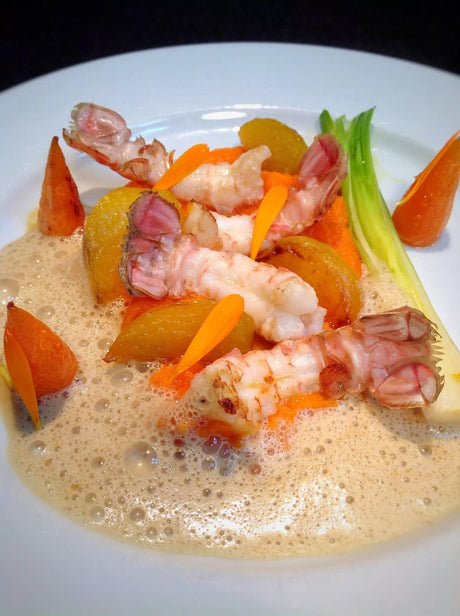 French langoustines with carrots, garden vegetables, and bisque foam on white plate