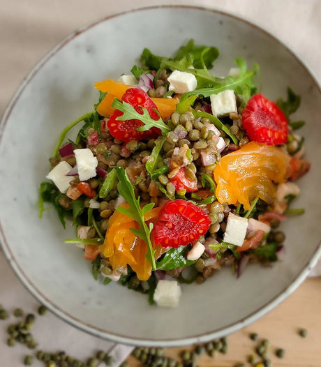 French green lentil salad with arugula, raspberries, cheese cubes, and yellow tomatoes in a bowl
