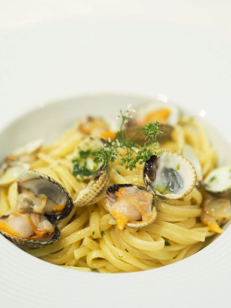 Linguini pasta with clams and herb garnish in a white bowl, French gourmet meal