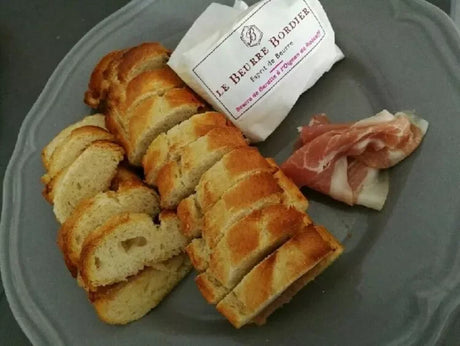 Sliced French baguette with Bordier butter and cured ham on a plate, premium French pantry product.