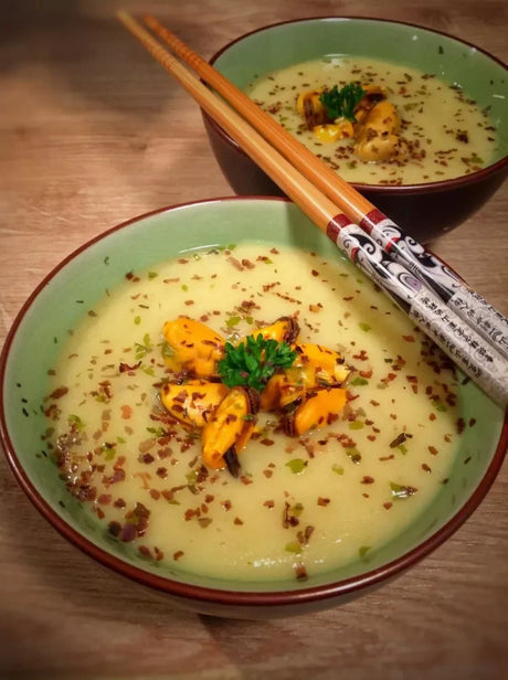 Potato and mussel soup garnished with herbs, featuring premium French butter, in green bowls