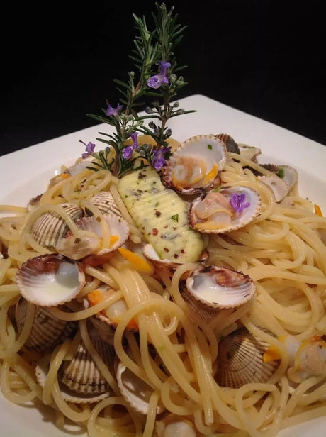 Spaghettini pasta with clams, Bordier seaweed butter, and rosemary on white plate