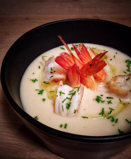 Velouté soup with shrimp, butter, onions, and herbs in a black bowl, French gourmet style.